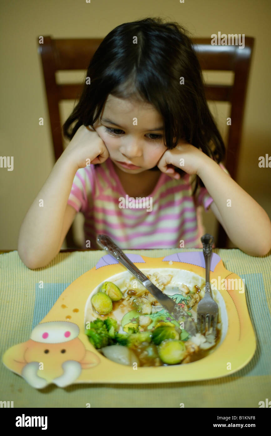 Jeune fille âgée de quatre peu disposés à terminer les légumes dans son assiette de rôti du dimanche soir Banque D'Images