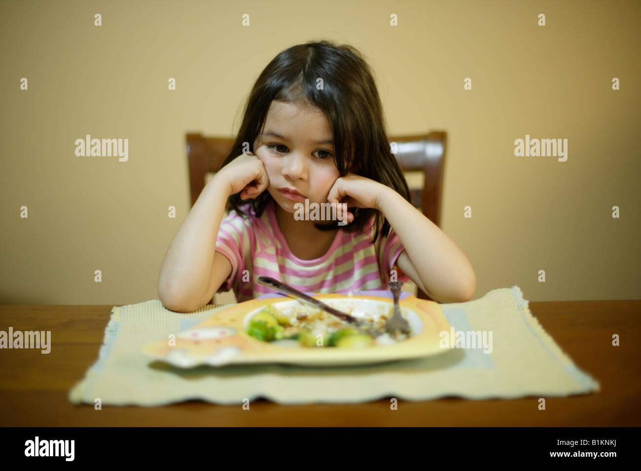 Jeune fille âgée de quatre peu disposés à terminer les légumes dans son assiette de rôti du dimanche soir Banque D'Images