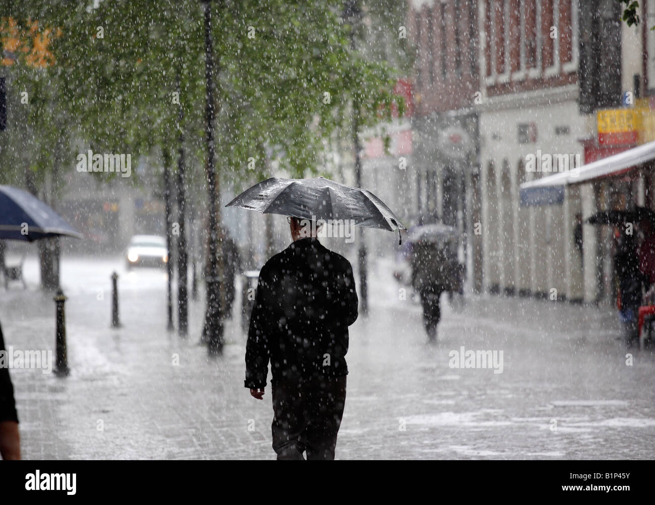 Un homme tenant un parapluie en marchant le long de High Street dans le Worcestershire Bromsgrove UK pendant une tempête de pluie Banque D'Images