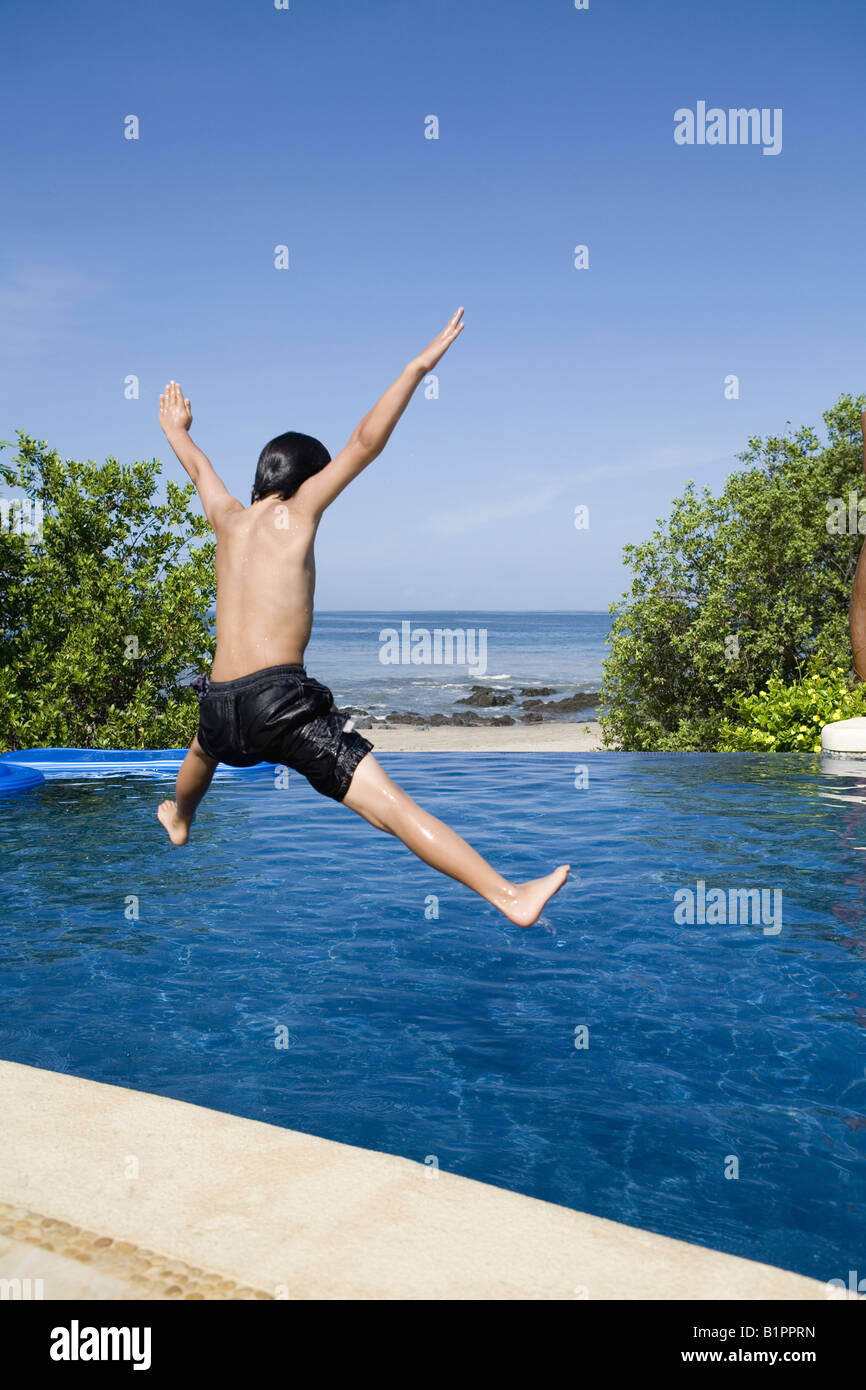 Jeune garçon sautant dans une jolie piscine à débordement avec vue sur l'océan Banque D'Images