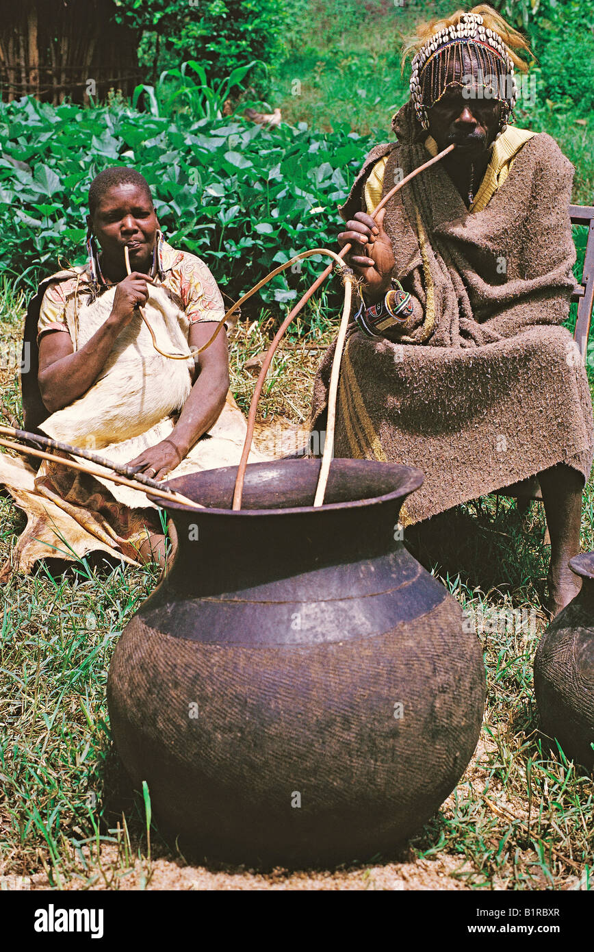 Nandi mari et femme prendre un verre de bière brassée à partir de la paille de mil aspiré via le Kenya Afrique de l'Est Banque D'Images