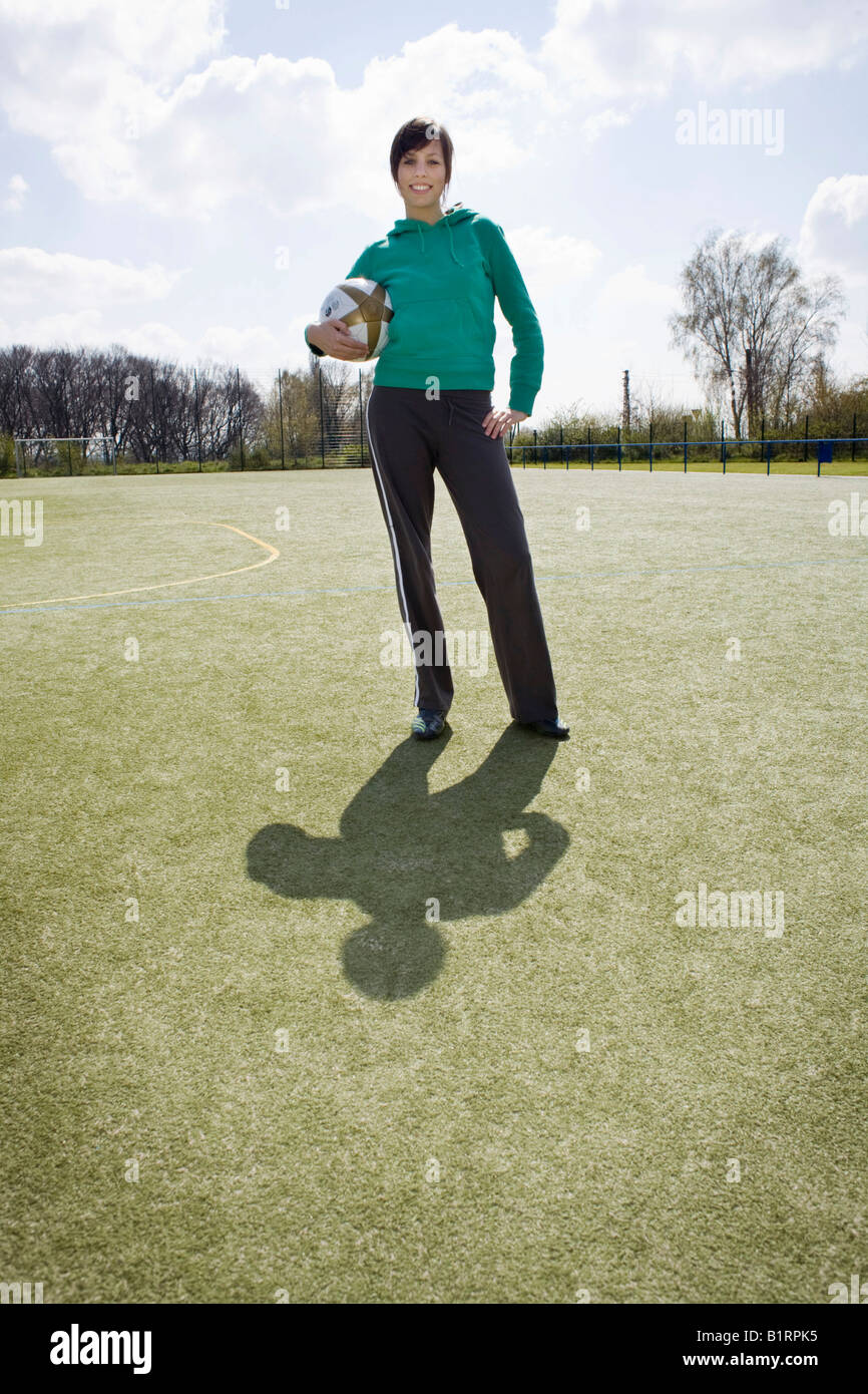 Jeune femme debout sur un terrain de sport holding a football Banque D'Images