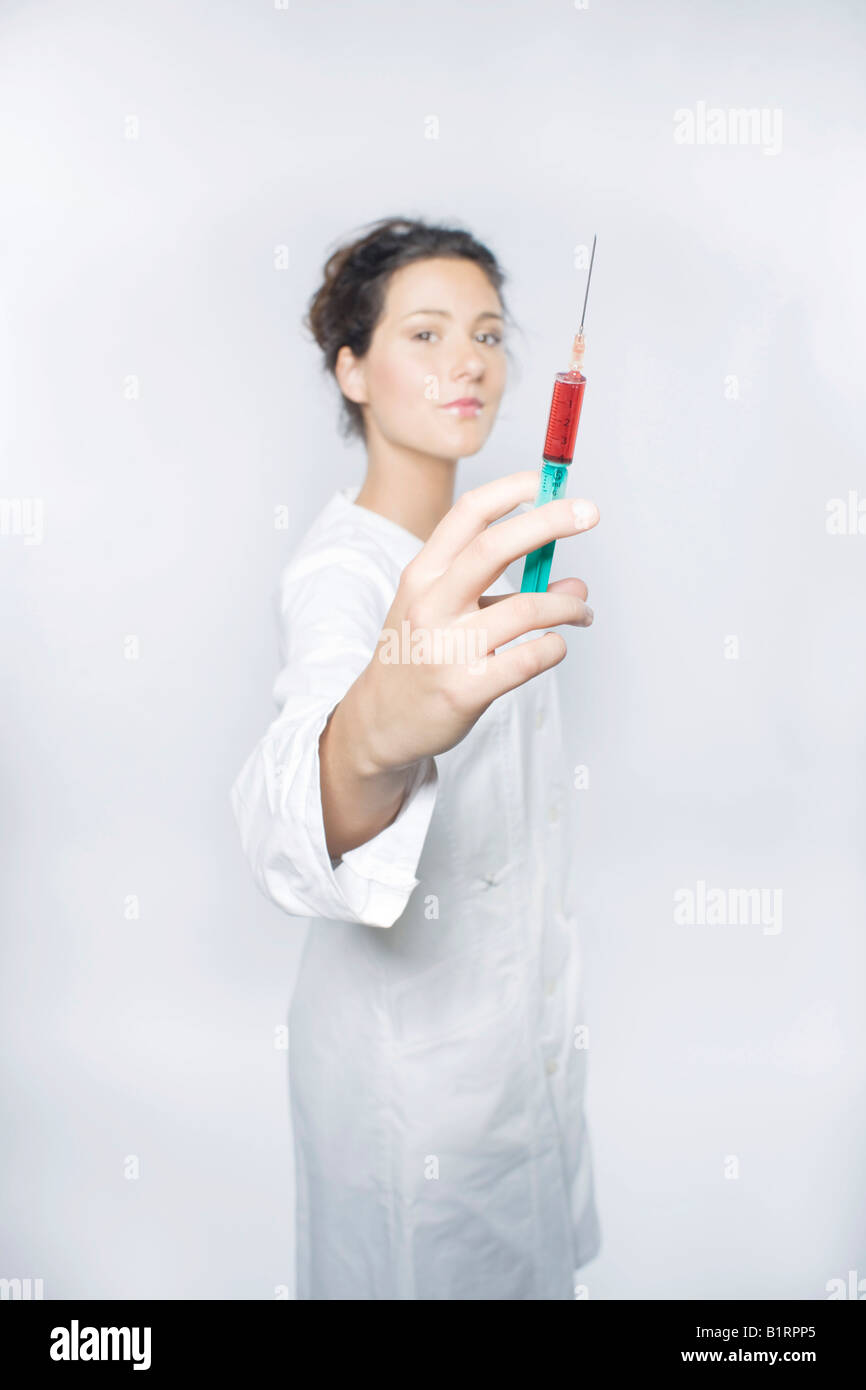 Jeune femme portant un sarrau de laboratoire blanc tenant une seringue remplie de liquide rouge vers l'appareil photo Banque D'Images