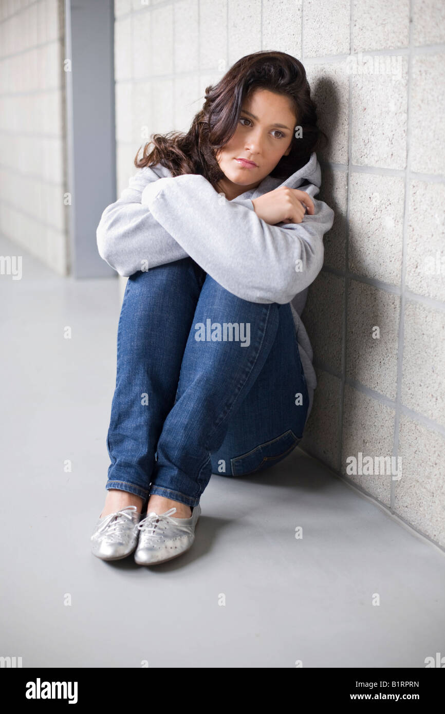 Jeune femme assise tristement sur le sol appuyée contre un mur Banque D'Images