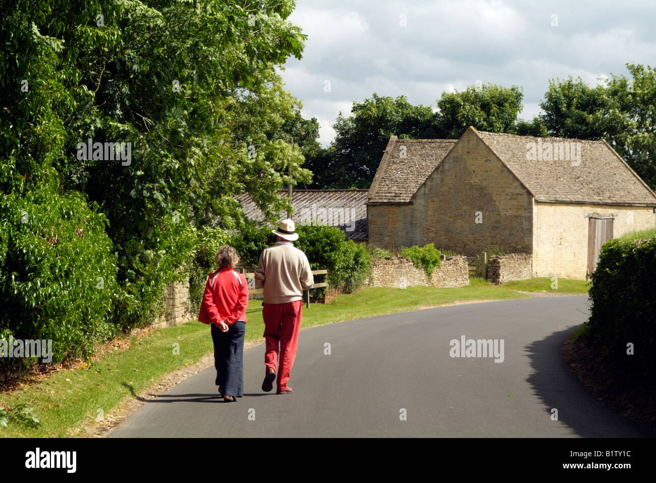 Couple walking through Guiting Power Cotswolds Gloucestershire Angleterre village Banque D'Images