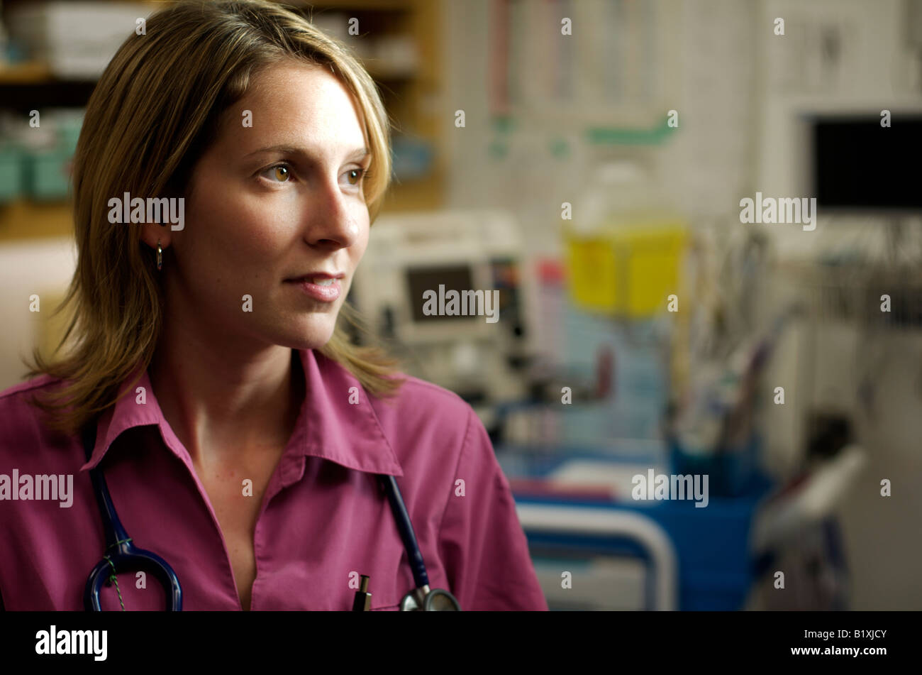 Infirmière dans scrubs dans un hôpital en souriant et posant avec un stéthoscope. Moitié du corps, posture. Poser sérieusement. Lumière dramatique Banque D'Images