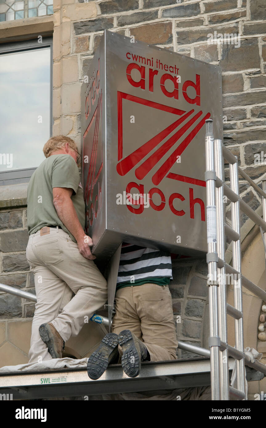 Deux hommes la fixation d'un metal sign au mur d'un bâtiment (Arad Goch theatre company, Aberystwyth, Pays de Galles UK) Banque D'Images