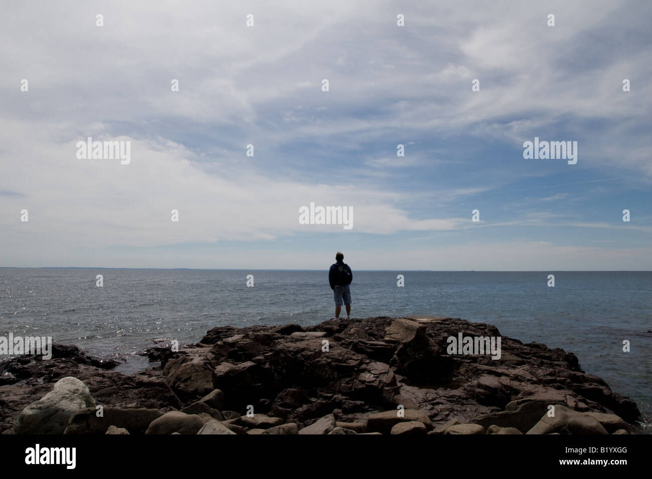 Un homme debout sur un rivage rocheux à la recherche à l'horizon. Banque D'Images