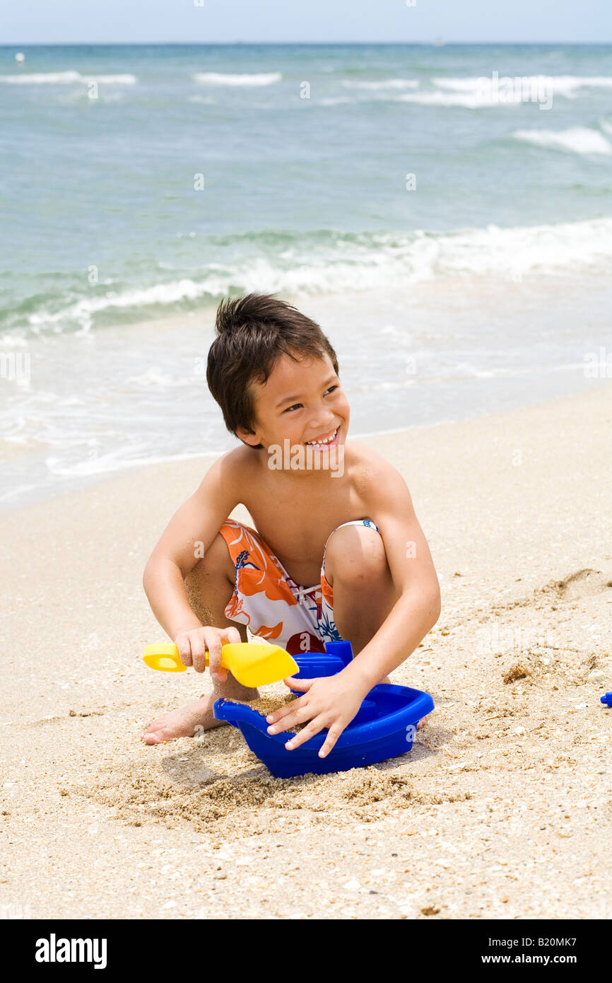 Jeune garçon (5-6 ans) à la suite de jouer avec les jouets de sable au bord de l'eau par la plage. Banque D'Images
