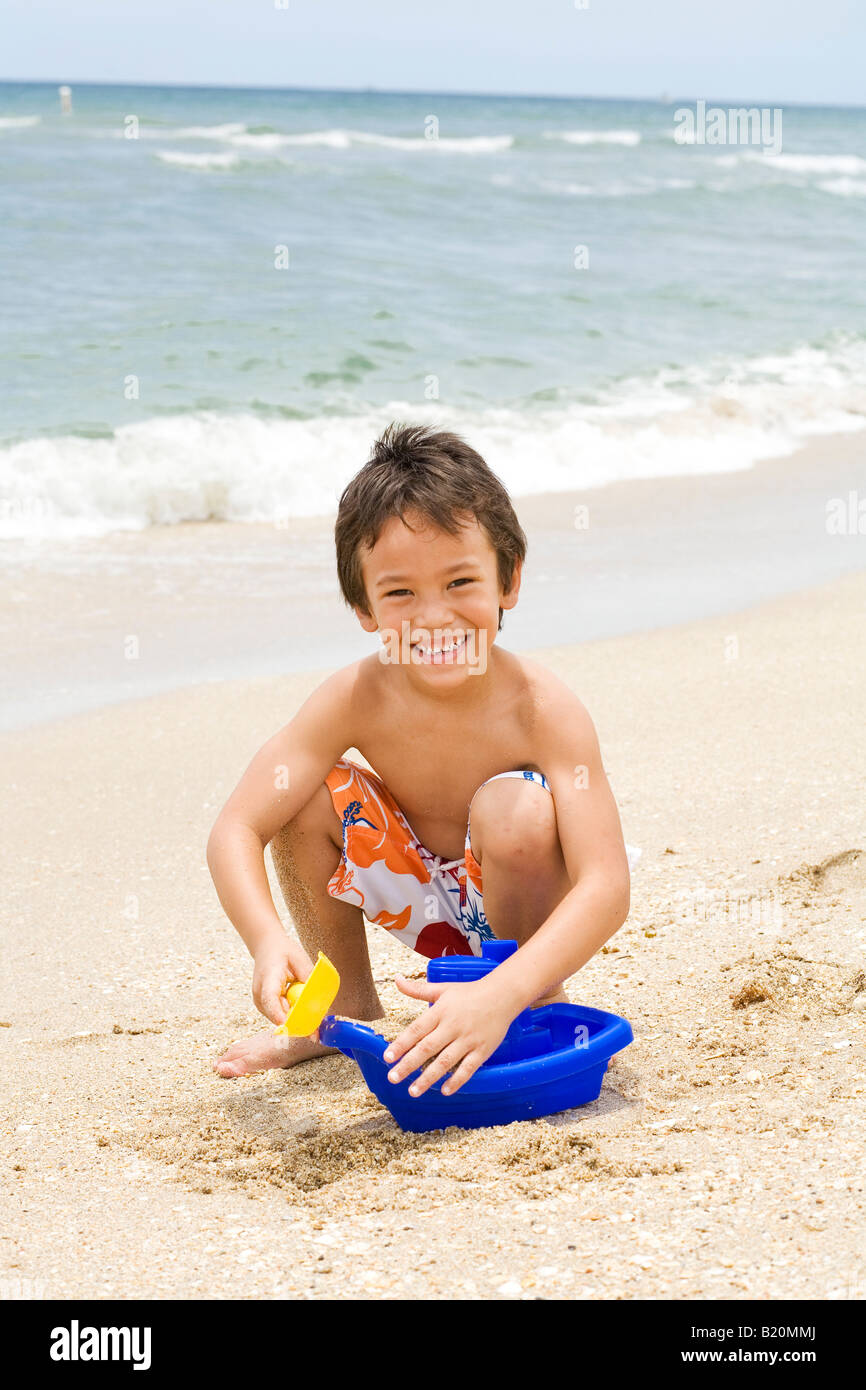 Jeune garçon (5-6 ans) avec les yeux à jouer avec les jouets de sable au bord de l'eau par la plage. Banque D'Images