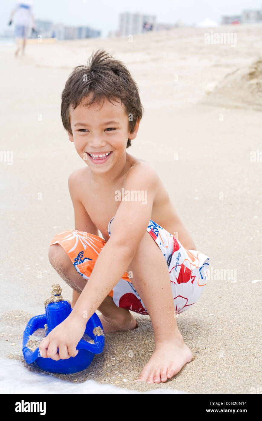 Jeune garçon (5-6 ans) avec les yeux à jouer avec les jouets de sable au bord de l'eau par la plage. Banque D'Images