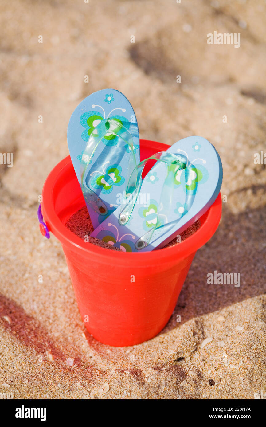 Paire de tongs bleu avec fleurs tourné en un seau en plastique sur la plage. Banque D'Images
