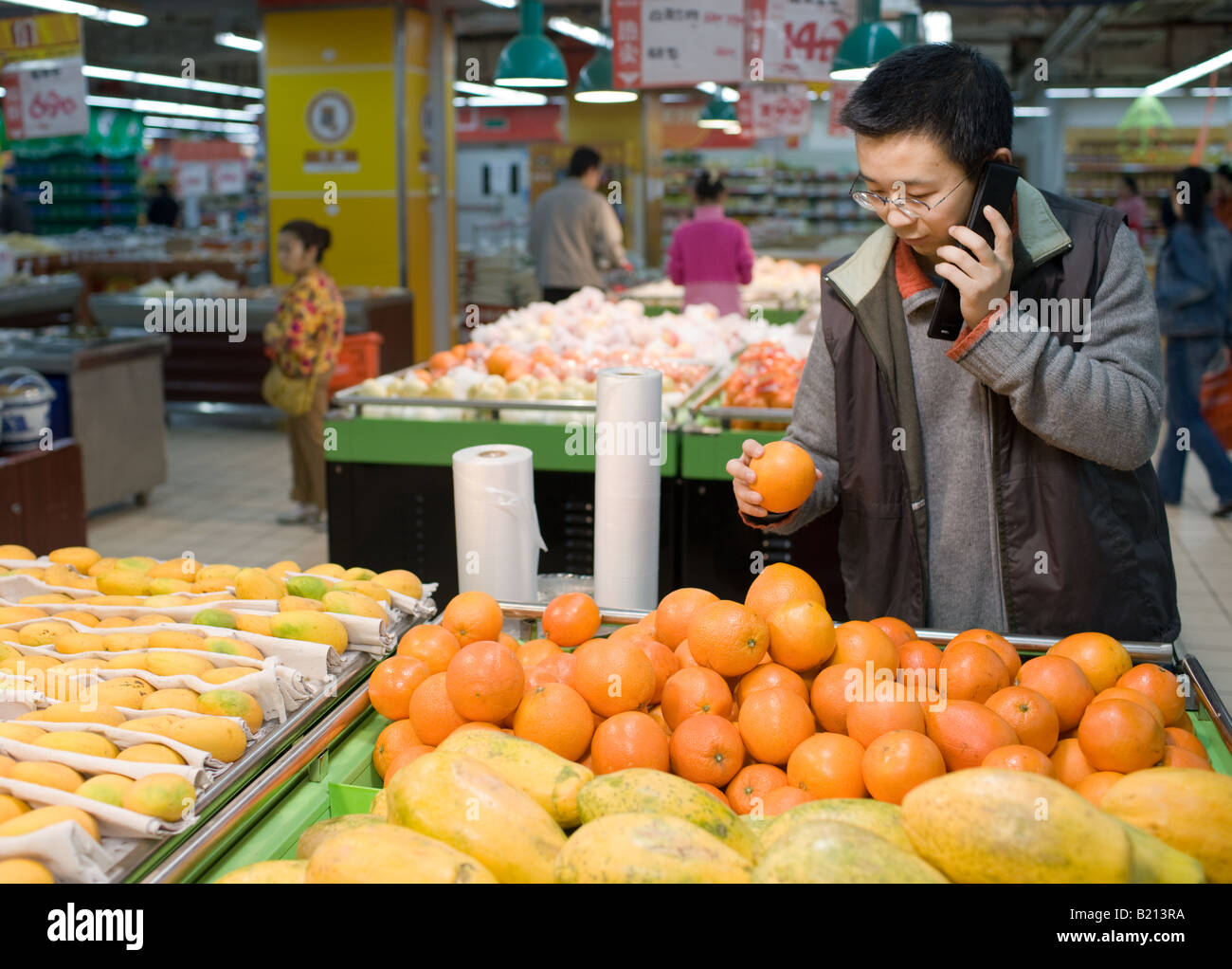 Jeune homme d'origine chinoise à l'aide de téléphone portable tout en choisissant des oranges en supermarché Chongqing Chine Banque D'Images