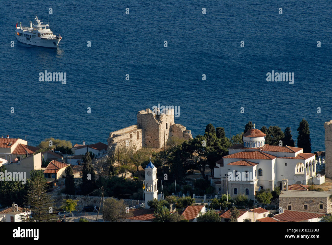 Château grec, église et maisons sur une colline au-dessus de la mer bleue avec un yacht à moteur à l'arrière-plan. Banque D'Images