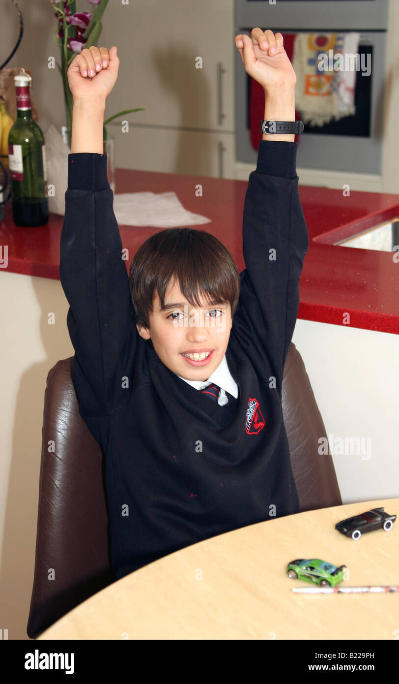 Portrait de jeune garçon enthousiaste brunette en uniforme d'cheering with arms raised at table de cuisine Banque D'Images