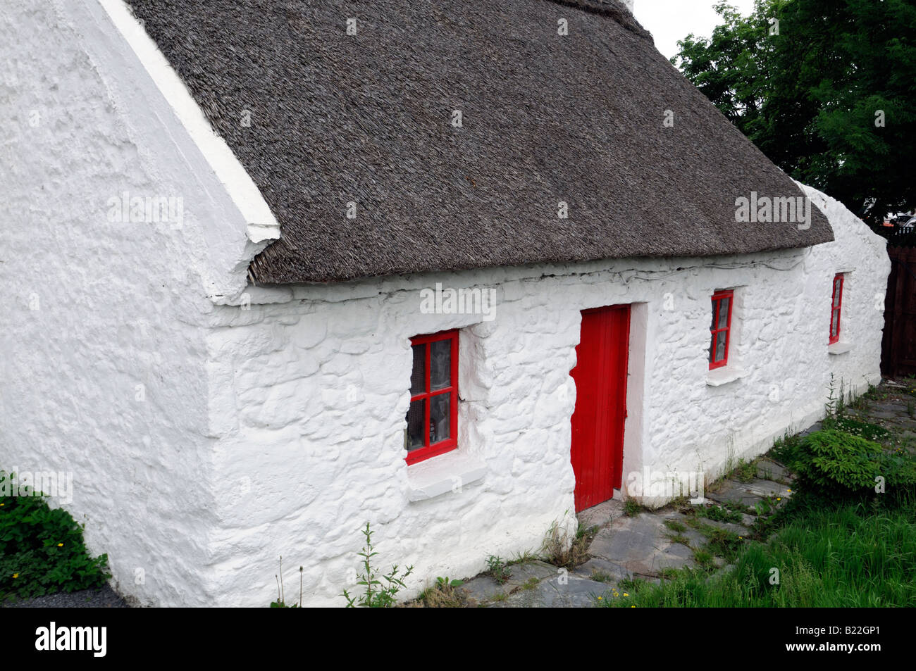 Cottage au toit de chaume avec porte en bois peint rouge et le cadre de la fenêtre maison traditionnelle en pierre peint en blanc Banque D'Images