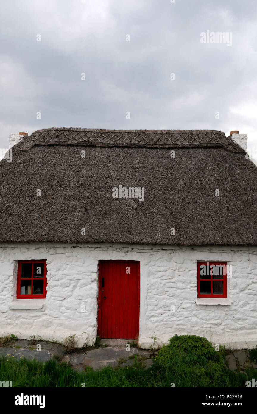 Cottage au toit de chaume avec porte en bois peint rouge et le cadre de la fenêtre maison traditionnelle en pierre peint en blanc Banque D'Images