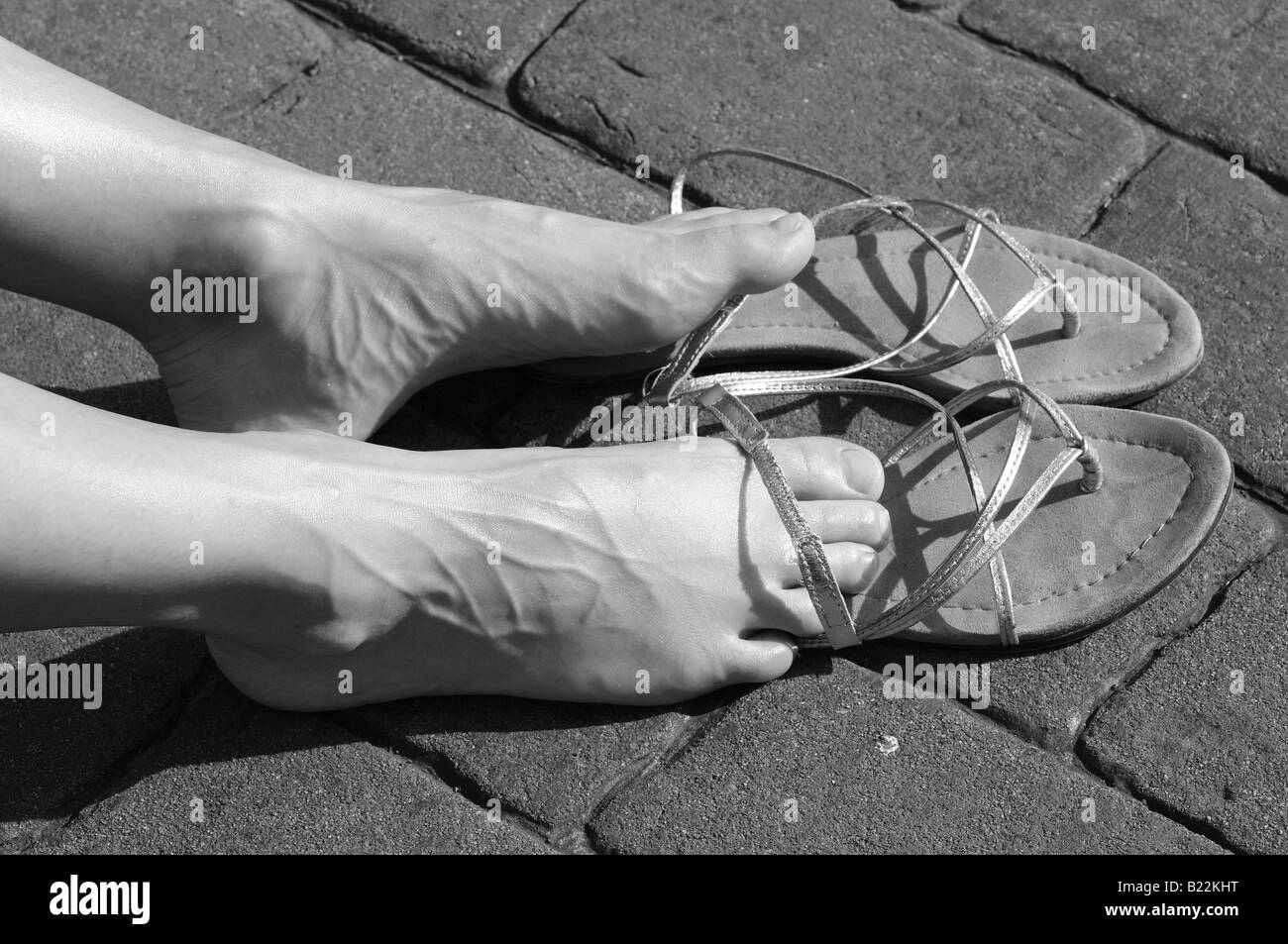 Les pieds de la femme et des sandales et elle prend le soleil sur le trottoir, en noir et blanc. Banque D'Images