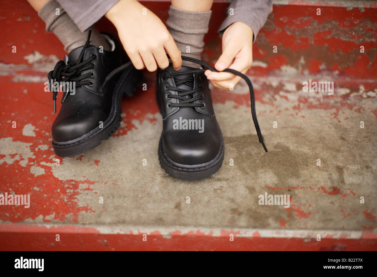 Six ans essaie d'attacher les lacets de ses nouvelles chaussures Banque D'Images