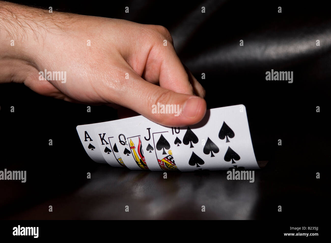 La main de l'Homme révélant la main de poker gagnante quinte flush royale dans des cosses sur fond noir Banque D'Images