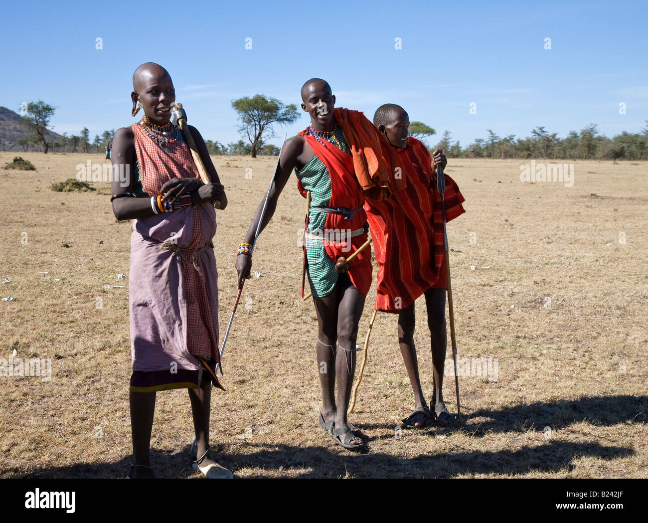 Les jeunes guerriers Masaï curieux et une femme près de leur village, situé dans le Masai Mara du Kenya Banque D'Images