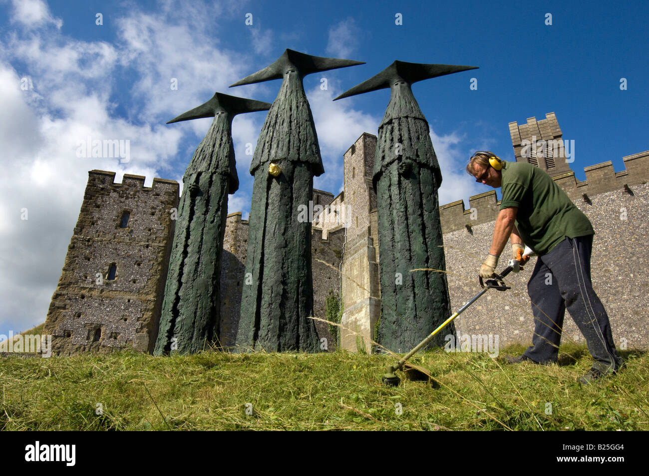 Un jardinier couper l'herbe autour des sentinelles, des sculptures de 'Philip Jackson' en face du château d'Arundel dans le Sussex. Banque D'Images