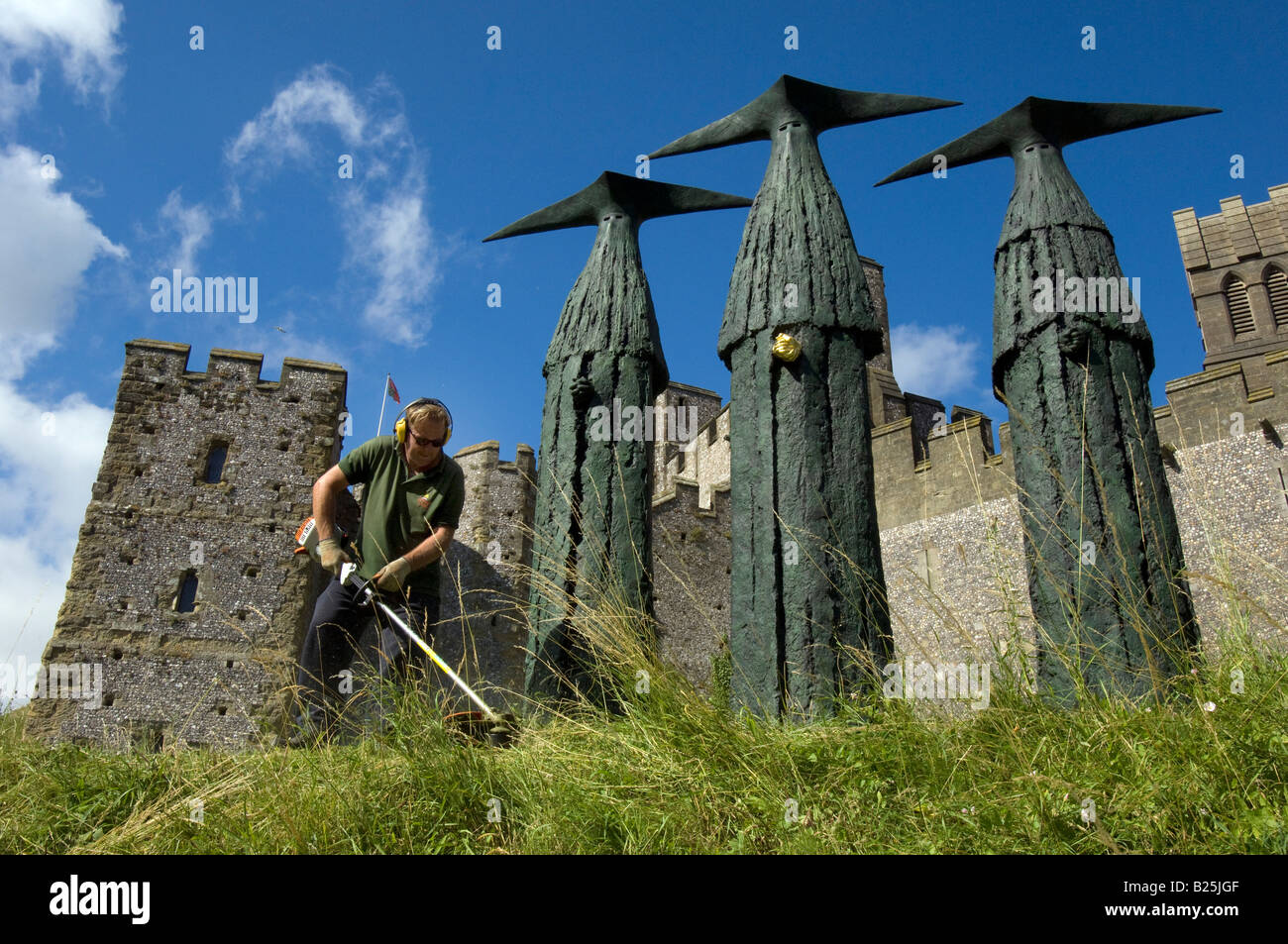 Un jardinier couper l'herbe autour des sentinelles, des sculptures de 'Philip Jackson' en face du château d'Arundel dans le Sussex. Banque D'Images