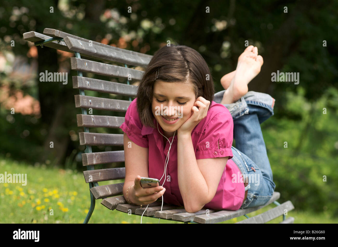 Jeune femme / fille de l'adolescence à l'écoute de la musique dans un parc étendu sur un banc Banque D'Images