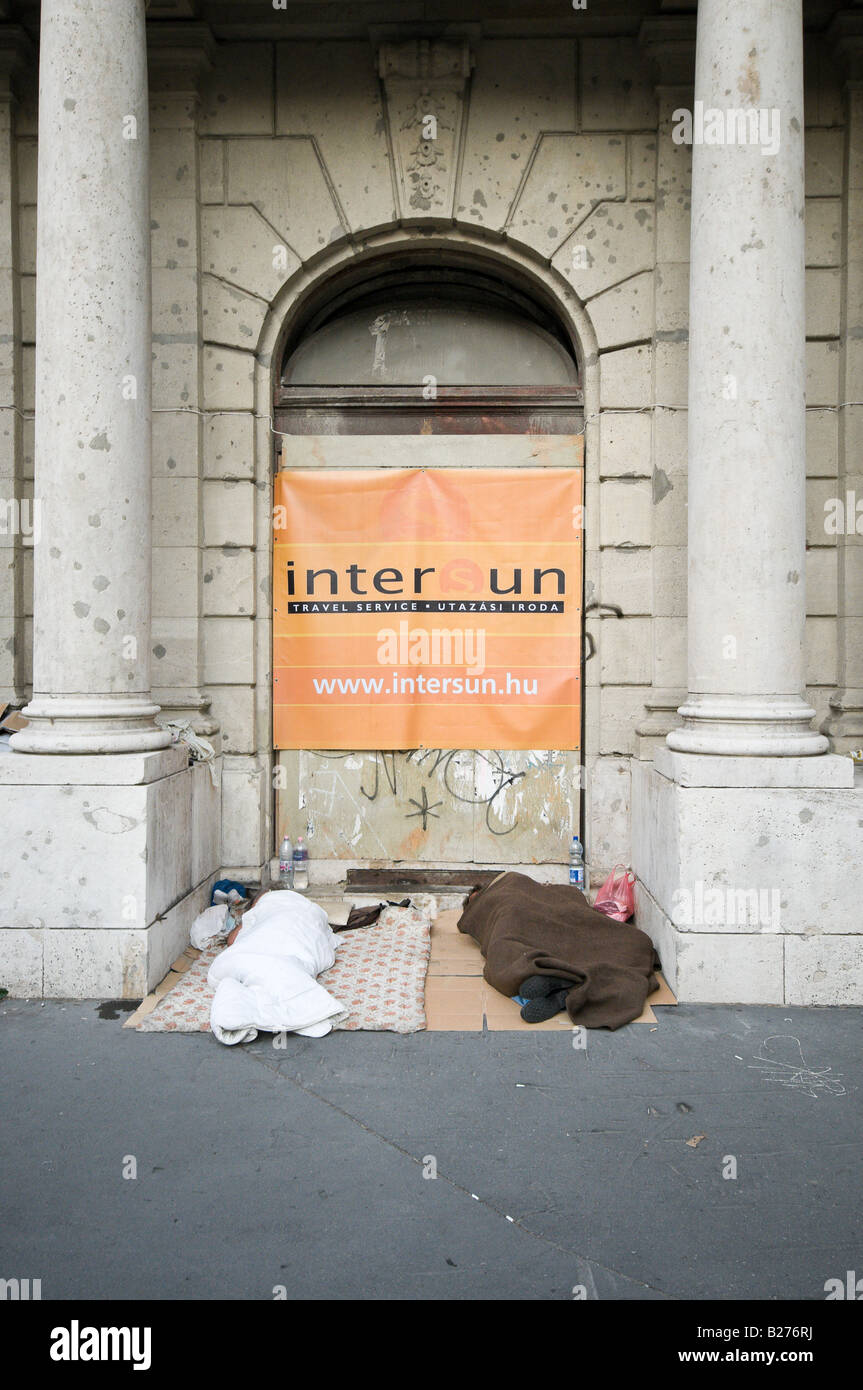 Deux sans-abri dormir dans une porte au-dessous d'une publicité signe cher les vacances. Banque D'Images