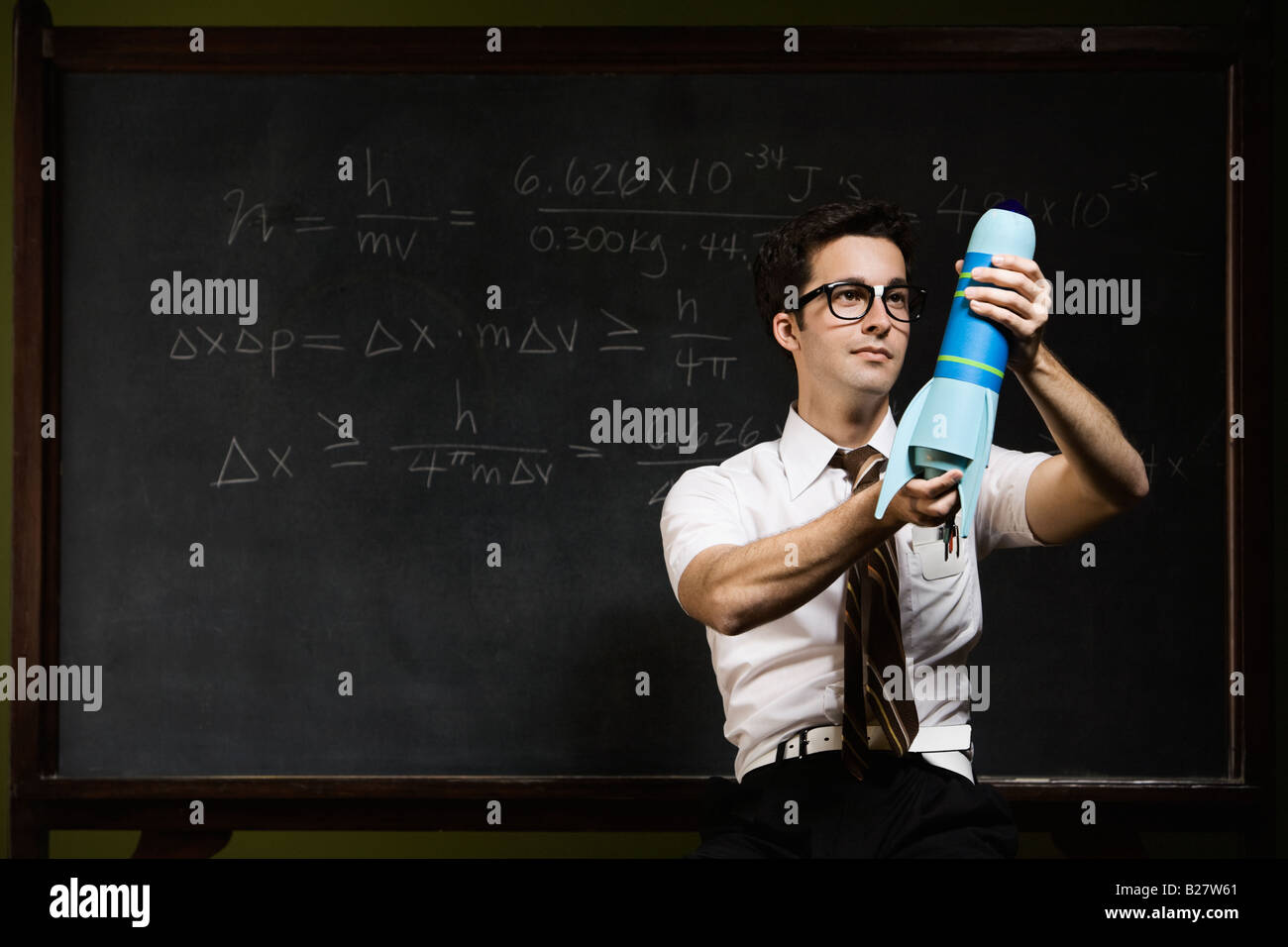Nerdy man holding rocket model in front of blackboard Banque D'Images