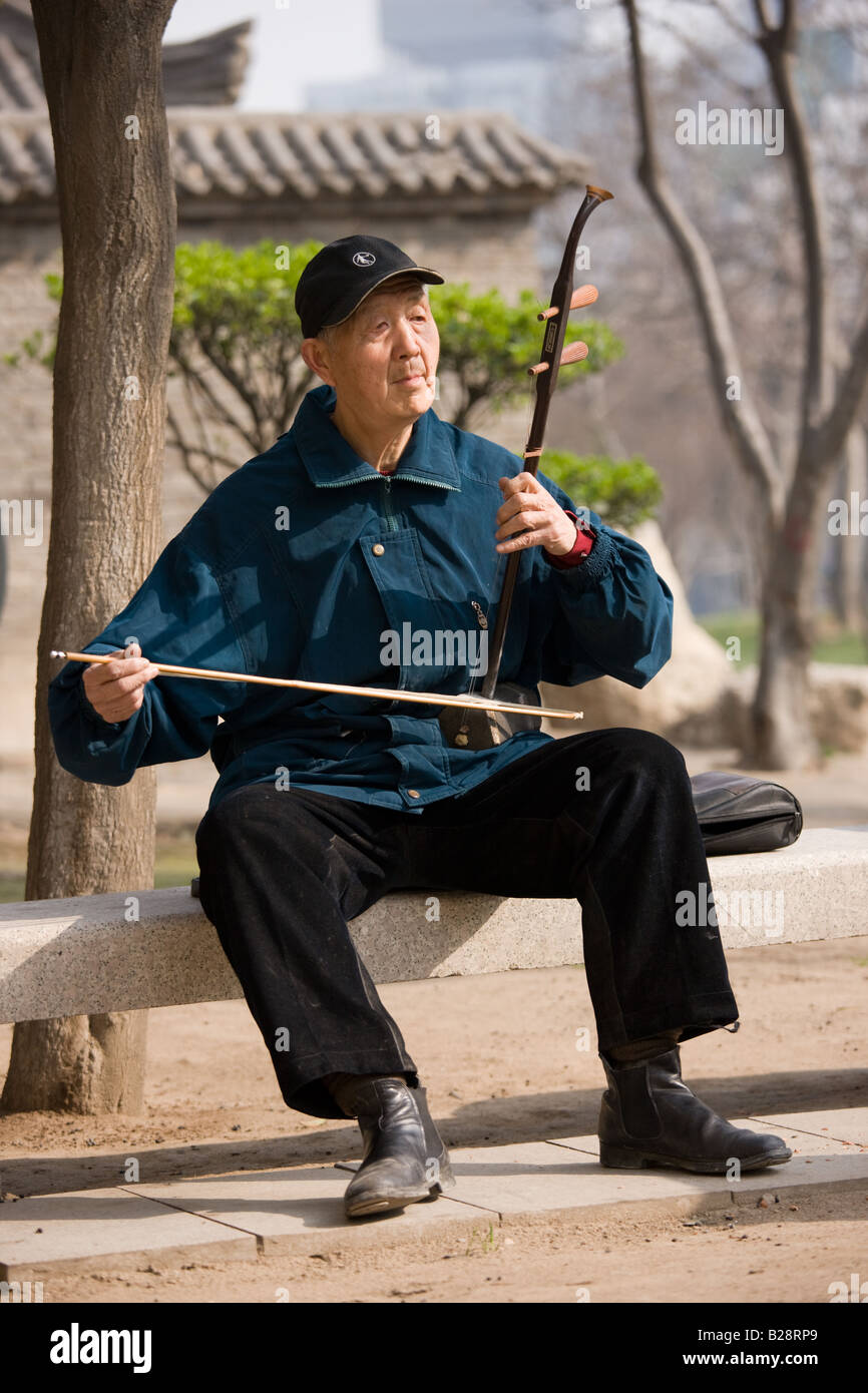 L'homme joue un Erhu, instrument à l'aide d'un arc dans le parc par le mur de la ville Xian Chine Banque D'Images