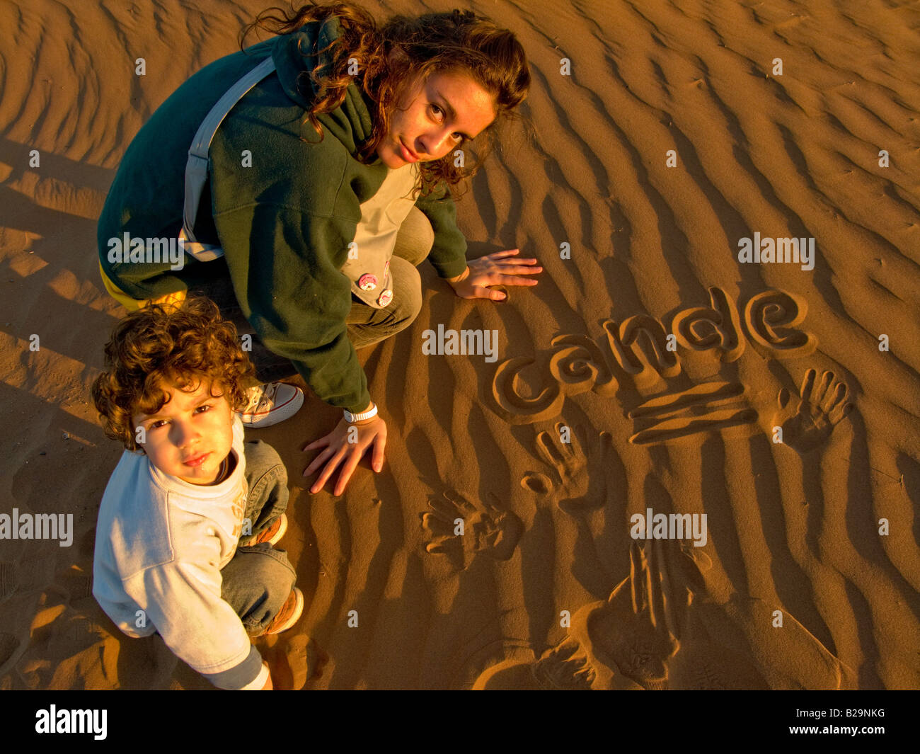 Frère et soeur de 3 et 13 ans de dessin et d'écriture sur une dune de sable au coucher du soleil Banque D'Images
