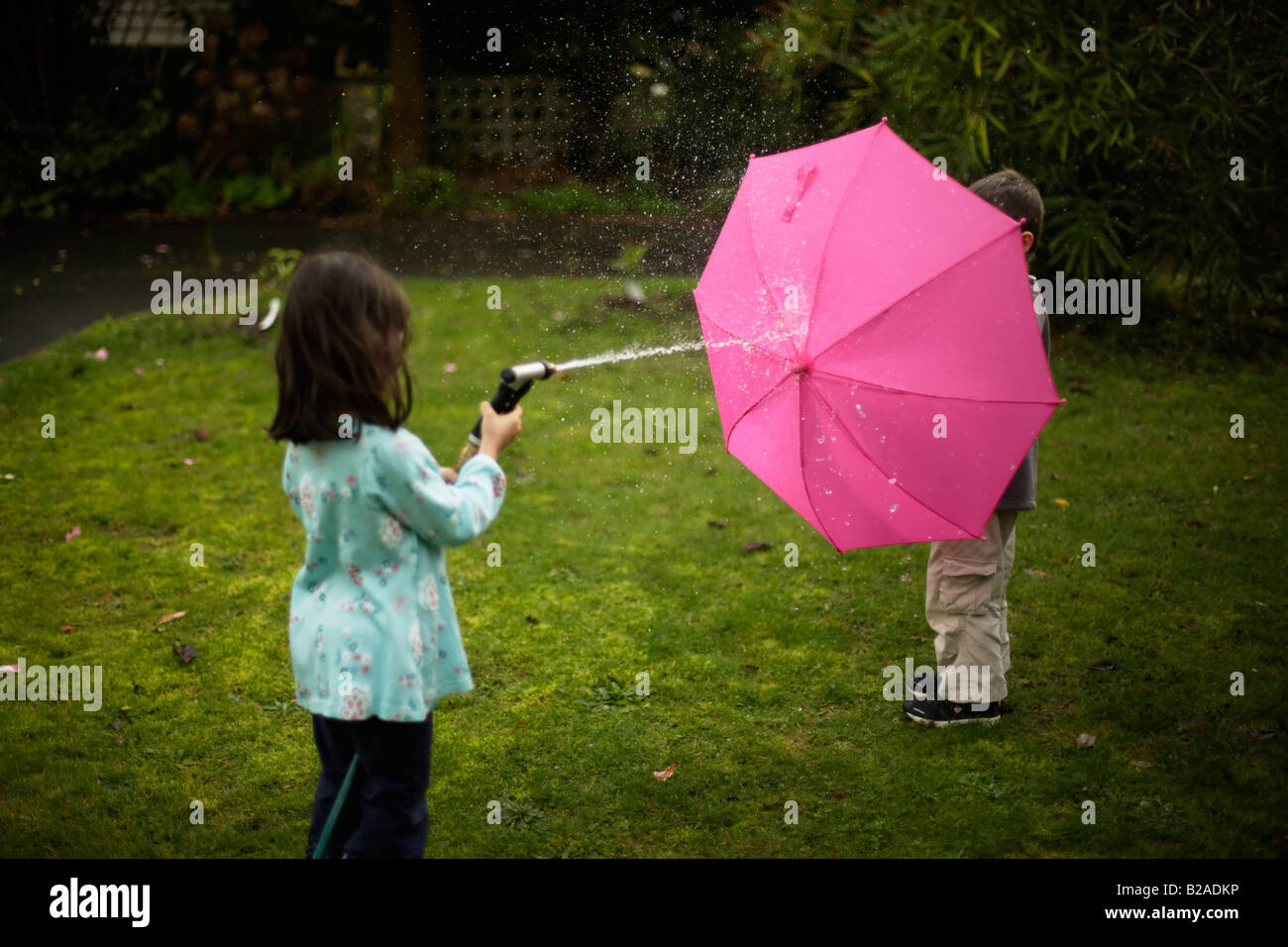 Garçon âgé de 6 ans se cache derrière un parapluie rose Banque D'Images