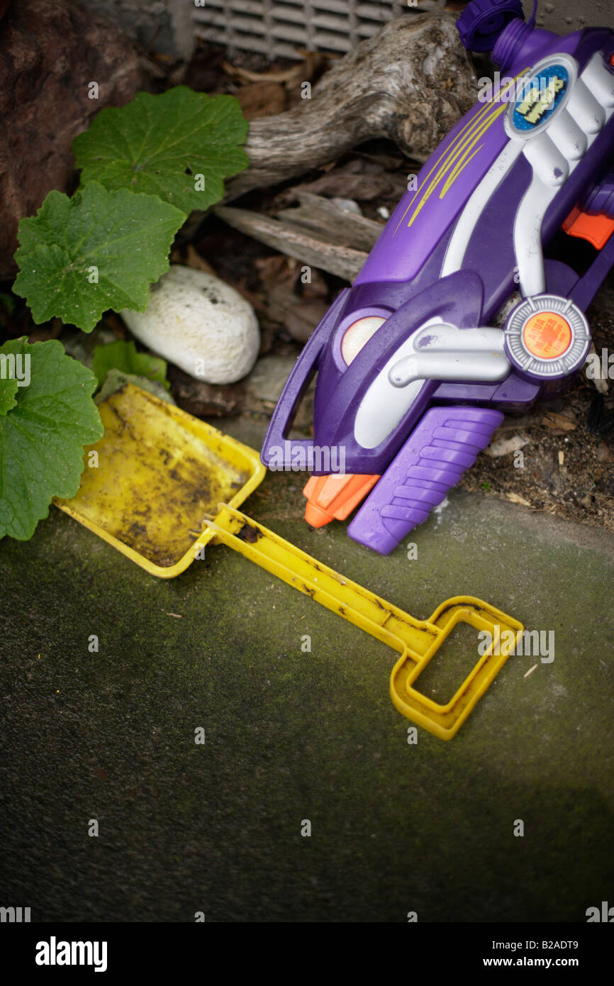 Pistolet à eau en plastique jaune et spade laissés sur le bord de chemin de jardin Banque D'Images