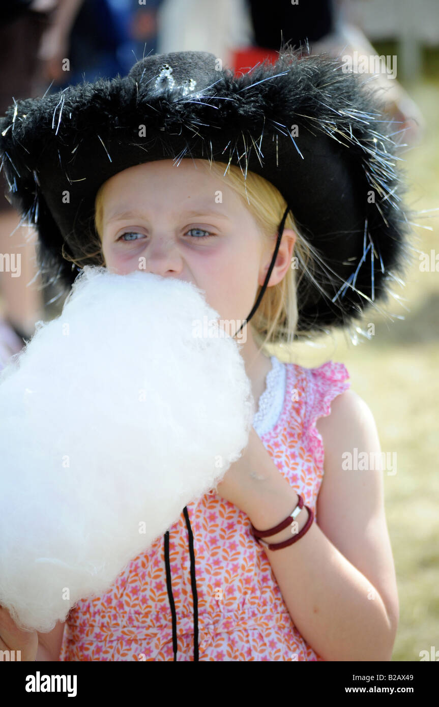 Image Photo d'une petite fille de manger de la barbe à papa à un festival de musique avec de cow-boy dans le soleil d'été London UK Banque D'Images