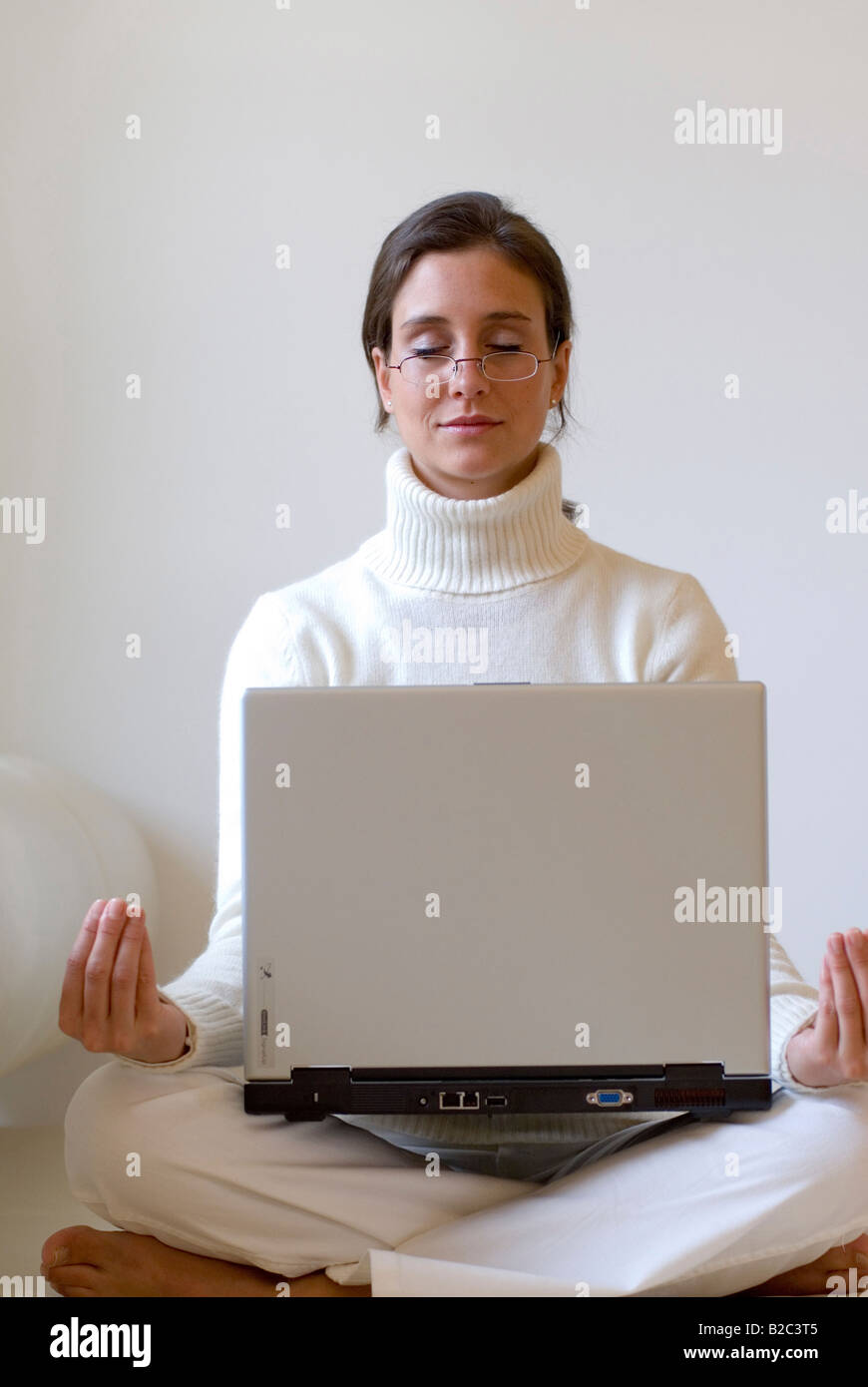 Jeune femme pratiquant le yoga avec un ordinateur portable sur ses genoux Banque D'Images Jeune femme pratiquant le yoga avec un ordinateur portable sur ses genoux Banque D'Images