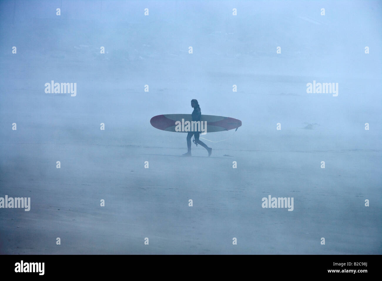 Surf femme boarder walking on foggy beach. Banque D'Images