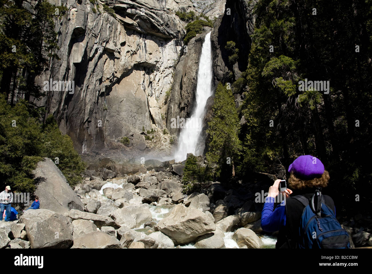 Un randonneur prend une photographie de Yosemite Falls inférieur comme une famille se détend sur certains des rochers géants du Yosemite. Banque D'Images