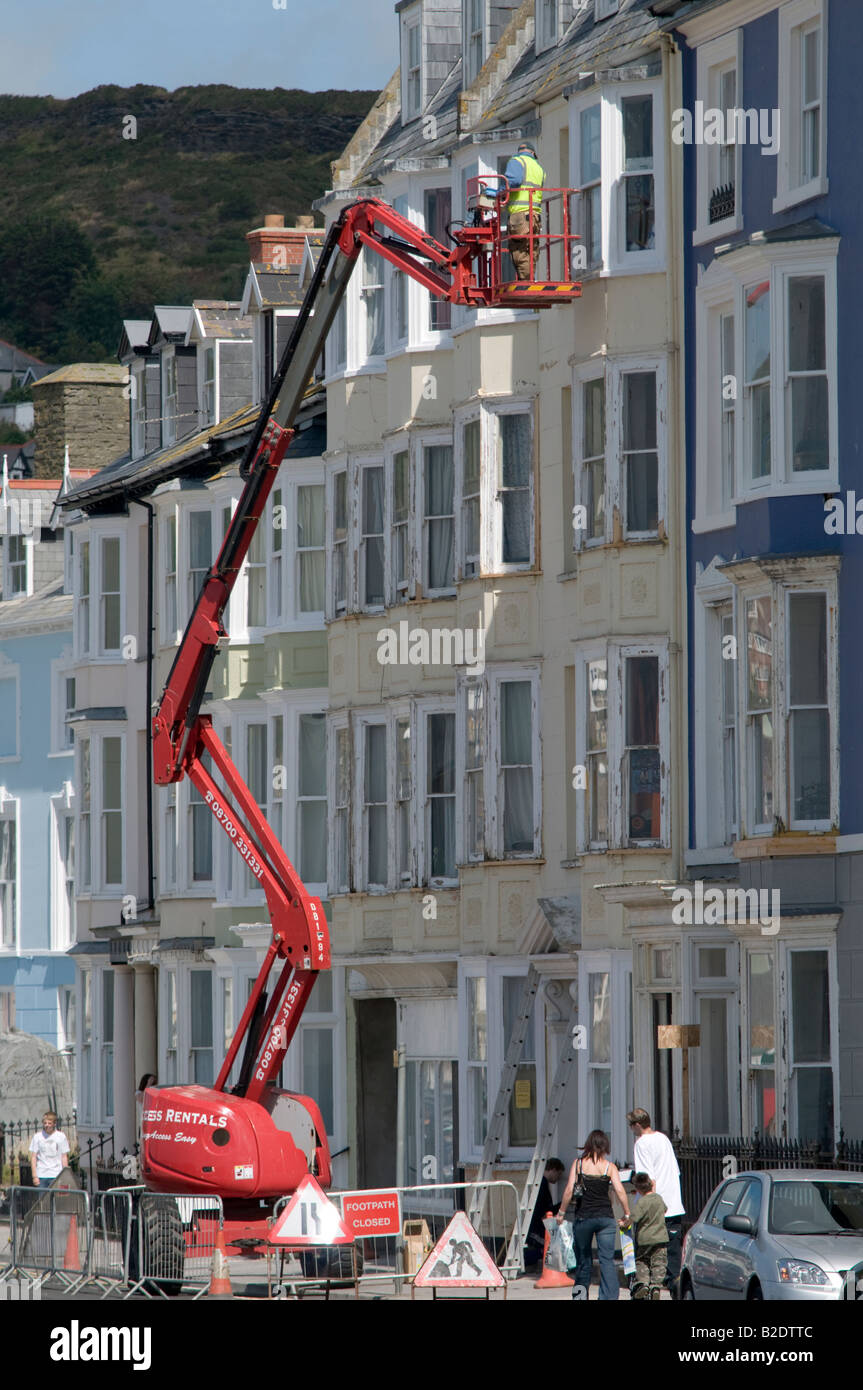 Man on cherry picker plate-forme surélevée, l'inspection de la façade des maisons en terrasse à Aberystwyth Wales UK Banque D'Images