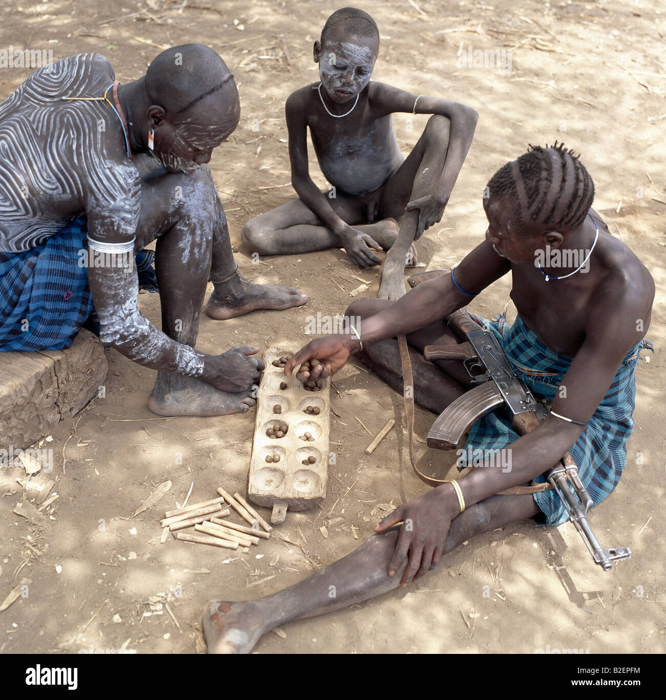 Deux hommes Mursi avec des modèles de jouer un jeu de bau comme un jeune garçon les regarde. Banque D'Images