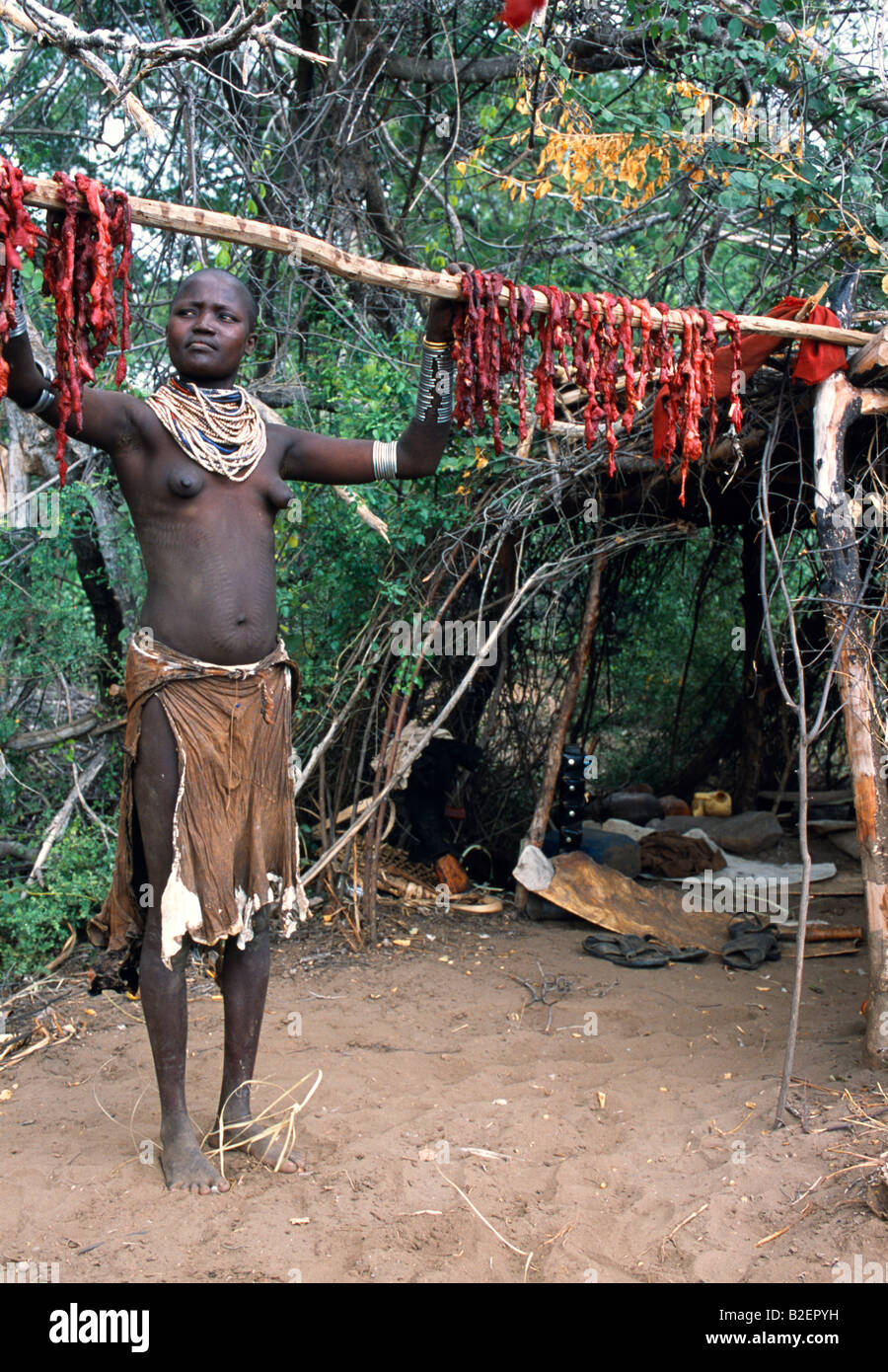 Une femme Karo se bloque à partir d'une viande de chèvre abattus à sécher sur un poteau à l'extérieur de son camp temporaire sur la rive de la rivière Karo. Une petite tribu Omotiques liés à l'Hamar, qui vivent le long des rives de la rivière Omo, dans le sud-ouest de l'Éthiopie, le Karo sont réputés pour leurs corps peindre à l'aide de craie blanche, la pierre concassée et d'autres pigments naturels. Banque D'Images