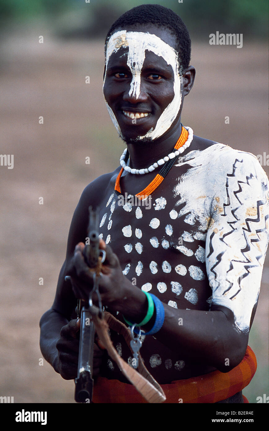 Un guerrier Nyangatom a peint son corps et visage en préparation d'une danse. La plupart des mâles adultes portent des fusils. Banque D'Images