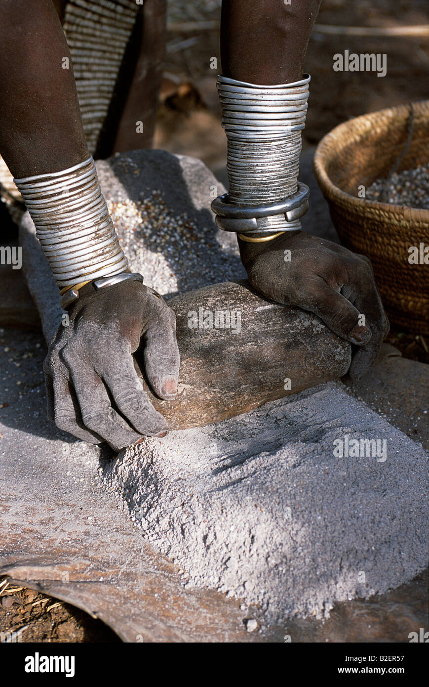 Une femme Nyangatom moud le sorgho à l'aide de deux pierres. Typique de sa tribu, elle porte une jupe en cuir perlé fortement. Banque D'Images