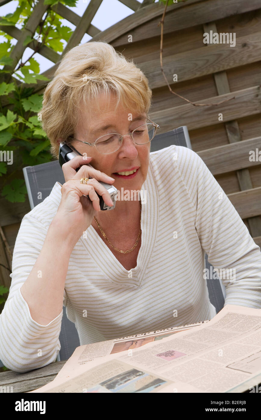 Femme PLUS ÂGÉE LECTURE PAPIER FINACIAL DANS JARDIN UK plusieurs valeurs Banque D'Images