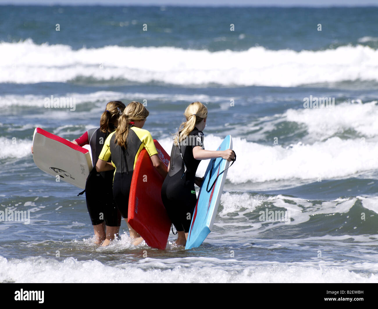 Trois jeunes filles portant des combinaisons et marcher dans la mer avec bodyboard Banque D'Images