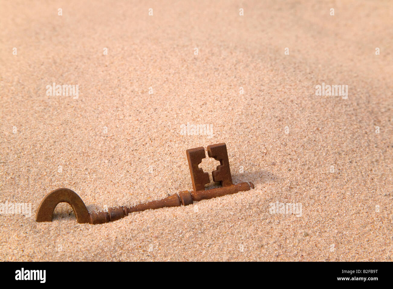 Une vieille clé rouillée partie enterrée dans le sable Banque D'Images