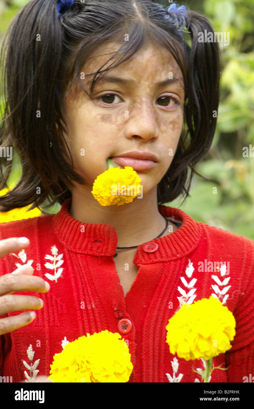 Une jeune fille indienne avec fleur jaune dans sa bouche en jouant le jardin faisant face à l'extérieur, Kalga funy, Inde 2007 Banque D'Images