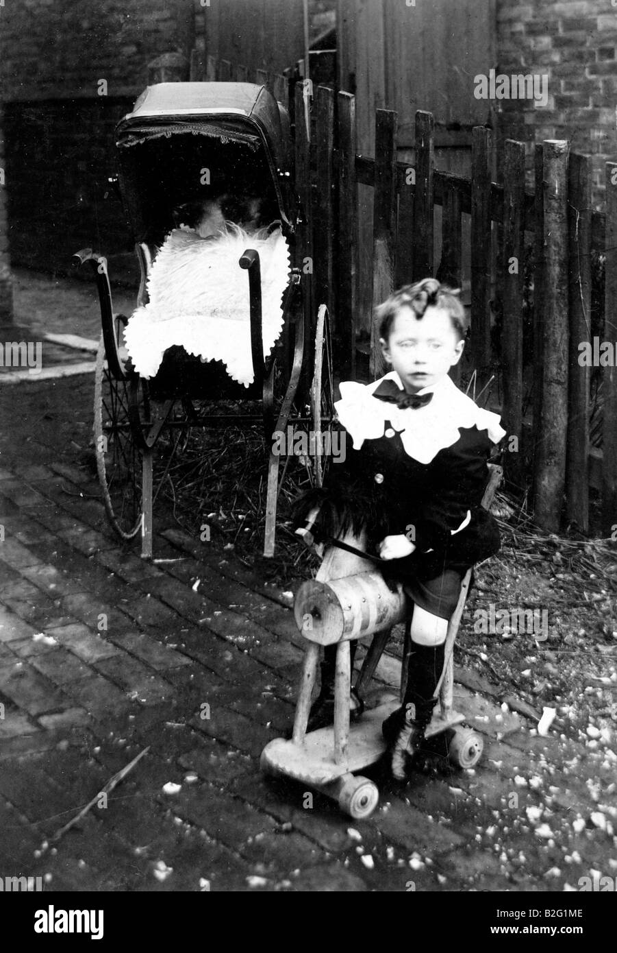 1905 photo édouardienne en noir et blanc d'un jeune enfant, garçon, 3-4 ans assis sur un cheval de loisir de type trolley dans le jardin. Pram en arrière-plan. Banque D'Images