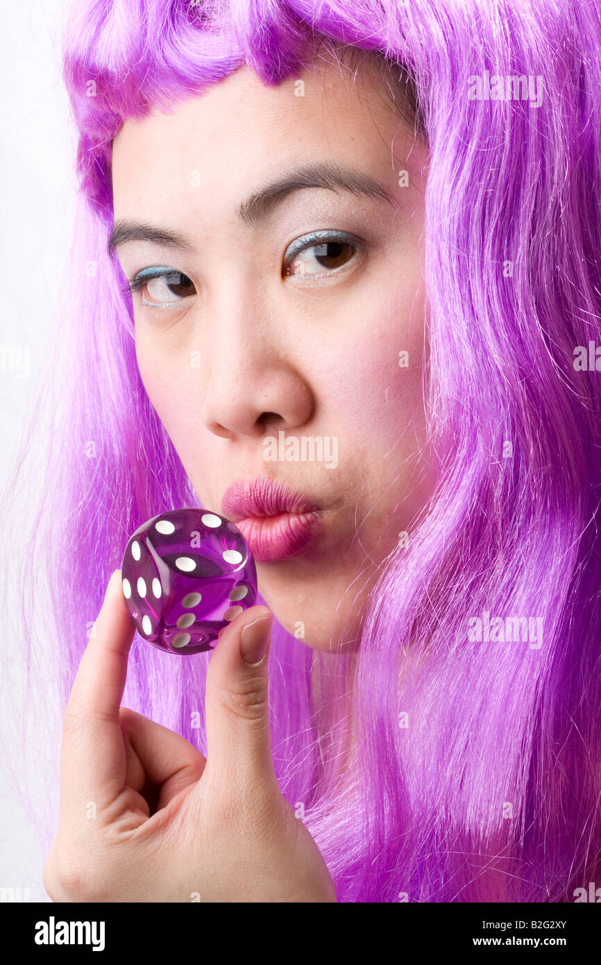 Une femme asiatique avec des cheveux violets, soufflant sur dice Banque D'Images