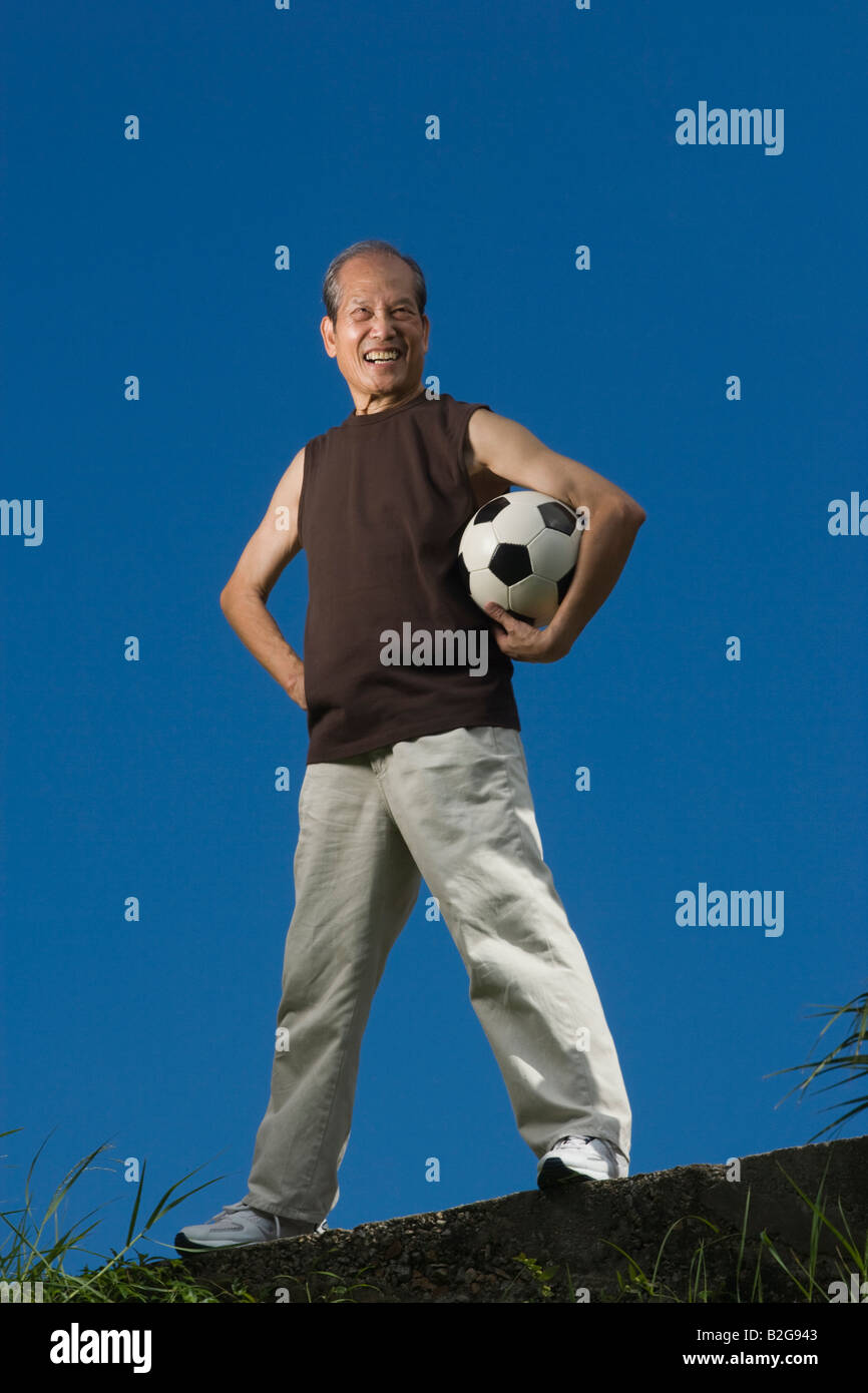 Low angle view of a senior man holding a ballon de soccer sous son bras et souriant Banque D'Images